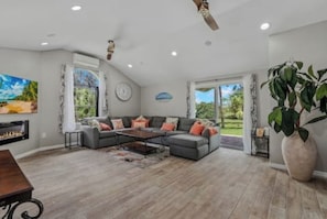 A spacious living room with a gray sectional sofa, a coffee table, a fireplace, and a large window. - 10 mins to Beach. 3bed/2ba pool home/game room. Private 1-acre. Pet friendly. (Englewood)