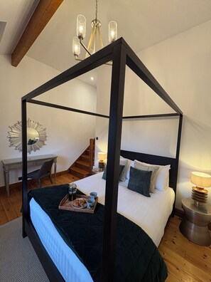 Ein Bett mit Baldachin, ein dunkler Rahmen, ein Schreibtisch mit Stuhl und eine Lampe auf einem Nachttisch.