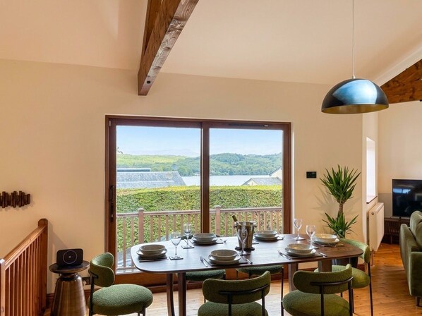 A dining area with a table set for four, large windows with a view of greenery, and a hanging light fixture. - Lake District Windermere Retreat with Lake Views (Windermere)