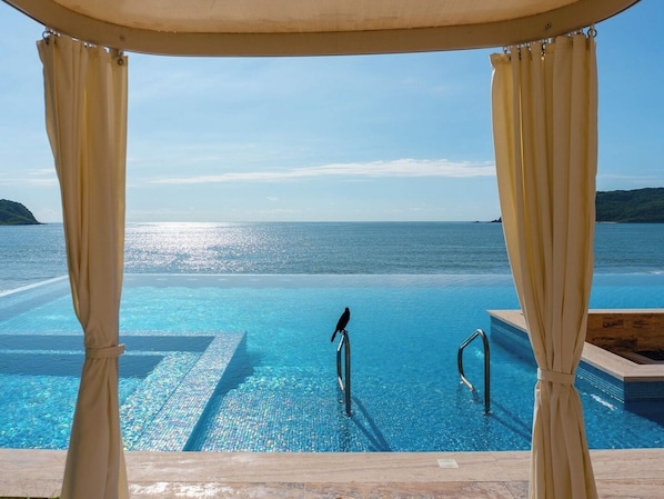 An infinity pool with a view of the sea, a bird on the edge, and a covered area with curtains. - ¡Apartamento de lujo frente al mar en Mazatlán! (Mazatlan)