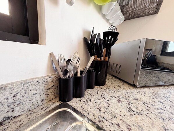 A kitchen with granite countertops, a sink, and utensils in holders.