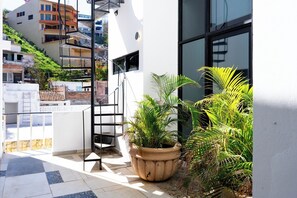 Un balcon doté d’un escalier, de plantes en pot et offrant une vue sur les bâtiments environnants.