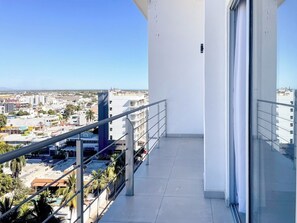 Un balcone con ringhiera metallica, una vista chiara sulla città e un muro bianco.