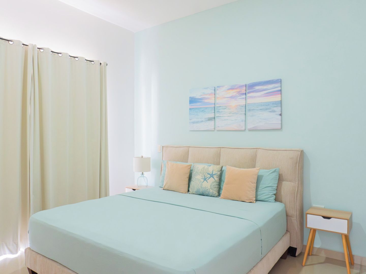 A bedroom with a bed, a nightstand, a lamp, and a small bedside table.