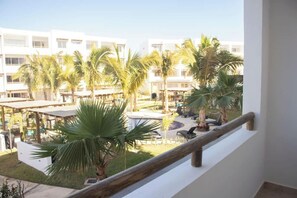 A balcony with a wooden railing overlooking a courtyard with palm trees and outdoor seating. - Departamento vacacional o de trabajo, 6 guest (Mazatlan)