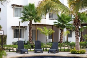 A poolside area with lounge chairs, palm trees, and a building with windows. - Departamento vacacional o de trabajo, 6 guest (Mazatlan)