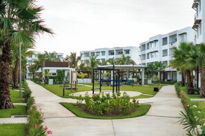 A hotel courtyard with a central seating area, surrounded by palm trees and a well-maintained lawn. - Departamento vacacional o de trabajo, 6 guest (Mazatlan)