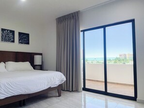 Una habitación de hotel con una cama, una mesita de noche, una lámpara, vistas al mar y un balcón.