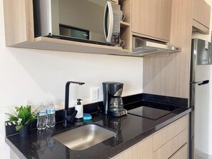 A modern kitchen with a black countertop, stainless steel sink, a coffee maker, and a microwave.