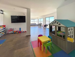 Un amplio espacio interior de juegos con una casita, un televisor de pantalla plana y almacenaje.
