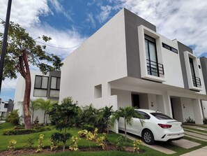 A modern two-story house with a white exterior, a car parked in the driveway, and a well-maintained garden with various plants. - House in Mezcales near Vallarta (Mezcales)