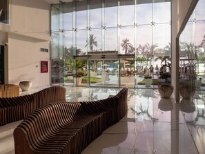 A modern lobby with a glass wall, a pool area, and seating. - Luxe Oceanfront Condo in Golden Zone (Mazatlan)