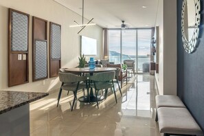 A modern dining area with a round table, chairs, and a view of the sea through large windows. - Luxe Oceanfront Condo in Golden Zone (Mazatlan)