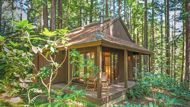 A cabin with a porch, wooden chairs, and a view of the forest.