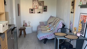 Ein gemütlicher Wohnbereich mit einer Couch, einem Esstisch mit Stühlen, einem kleinen Hocker und einem Spiegel.