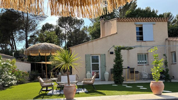 Ein Poolbereich mit Terrasse, Stühlen, einem Tisch und einem Haus mit Ziegeldach.