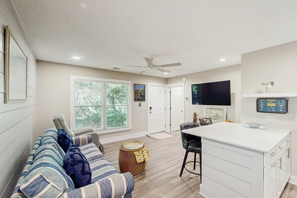 A modern living room with a sofa, a dining area with a white table, and a kitchen with a white cabinet.