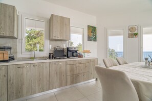 Una cocina moderna con armarios de madera, un comedor con mesa y sillas, y vistas al mar a través de las ventanas.