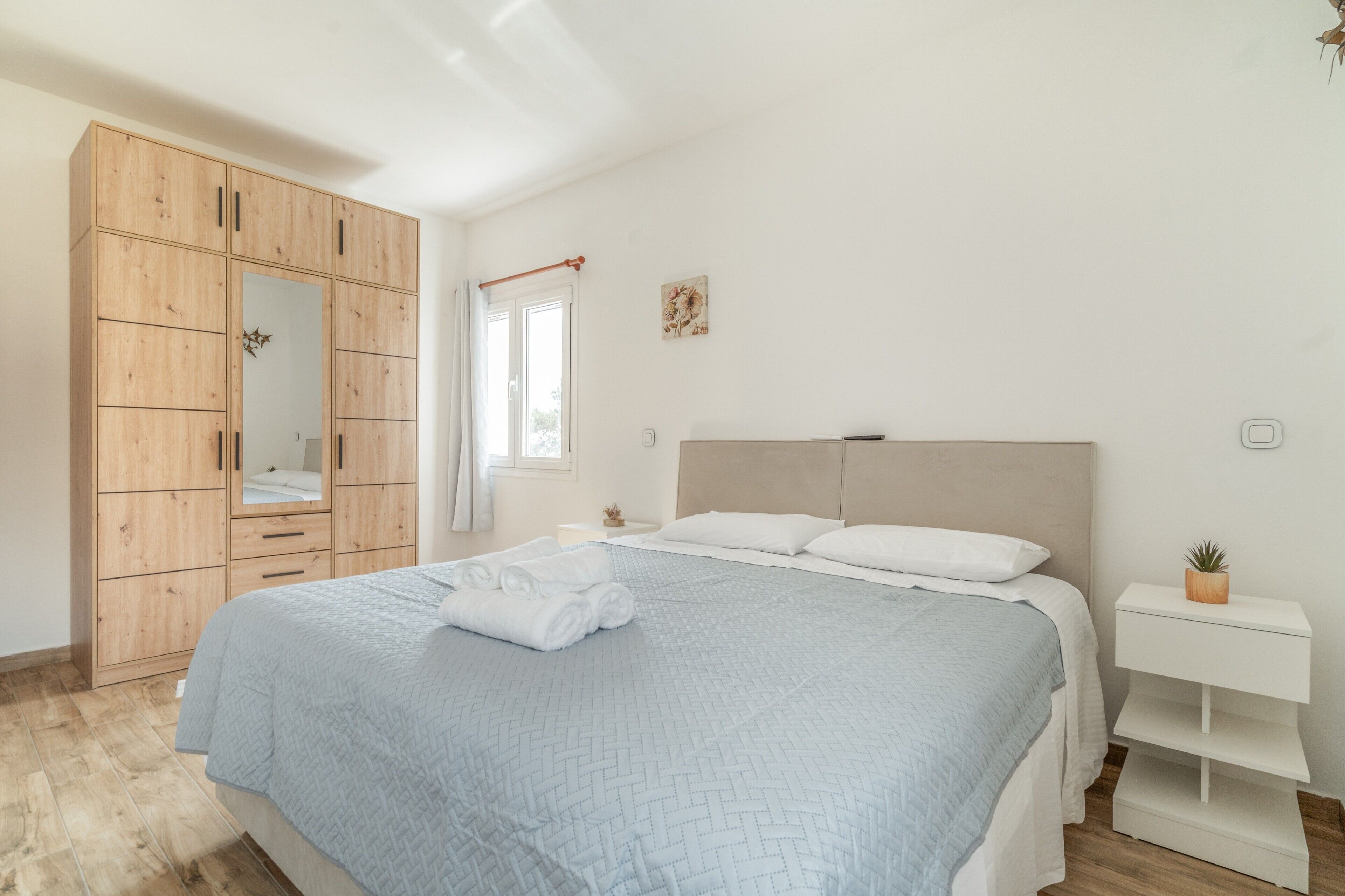 A bedroom with a bed, wooden wardrobe, bedside table, and a small potted plant.