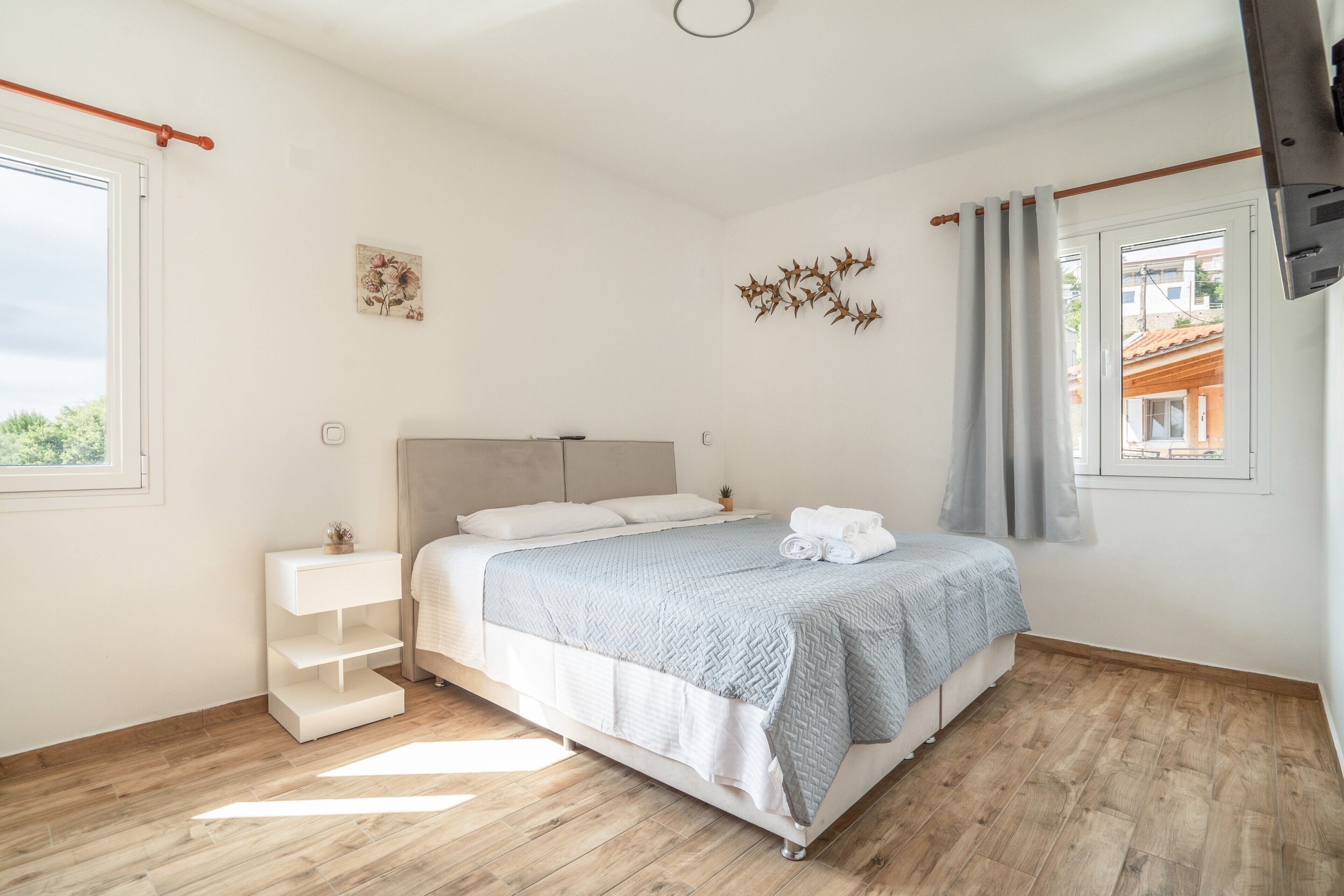 A bedroom with a bed, a bedside table, a wall-mounted TV, and a window with curtains.
