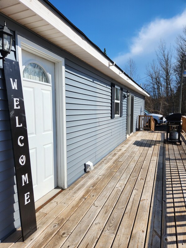 Ein Haus mit einem 'WELCOME'-Schild, einer Garagenöffnung und einer Holzterrasse.