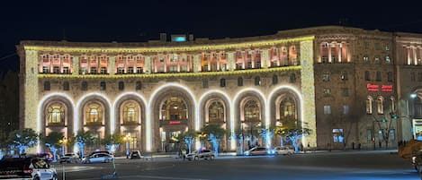 A large building with arched windows and a Marriott sign, surrounded by a well-lit plaza with trees and parked cars.