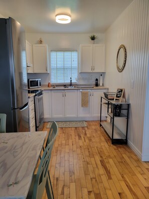 A kitchen with white cabinets, a microwave, a refrigerator, a sink, and a dining table with chairs.