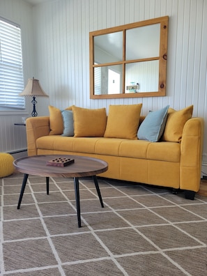 A yellow sofa with a wooden frame, a round coffee table, a lamp, and a mirror on the wall.