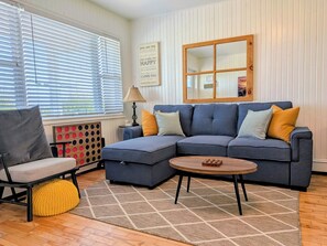 A living room with a sectional sofa, a round coffee table, a chair, and a patterned rug. - Cozy Cottage with the Big Deck! (Brackley Beach)
