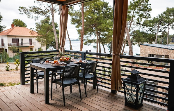 Eine Holzdar Terrasse mit einem für das Frühstück gedeckten Tisch, mit Blick auf ein Gewässer und Bäume.