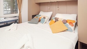 A neatly made bed with white linens, a rolled towel, and colorful pillows.