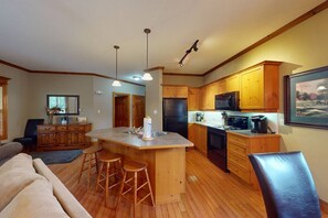 A spacious kitchen with wooden cabinets, a central island with stools, a refrigerator, microwave, and a coffee maker. - 2BD Condo, Mins to Village w/ Summer Pool (The Blue Mountains)