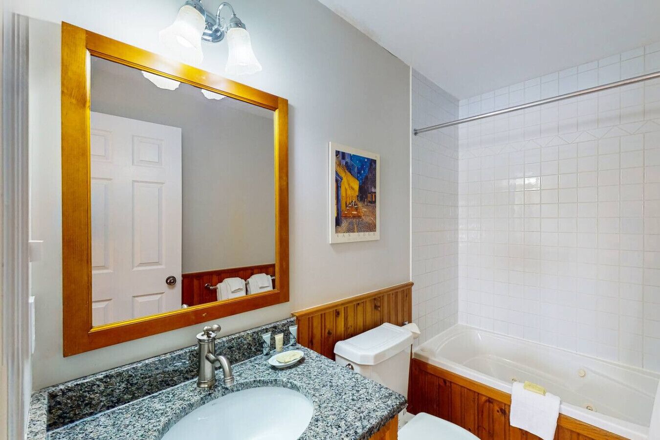 A bathroom with a granite sink, a large mirror, a shower, and a framed picture on the wall.