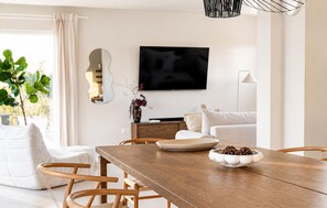 A modern living room with a wooden dining table, white sofas, a flat-screen TV, and a potted plant. - Gorgeous home in Policnik (Policnik)