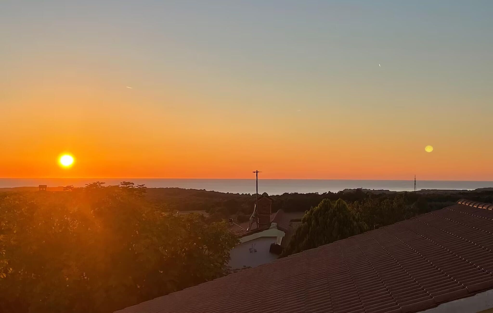 Solnedgang over et kystlandskab med et hus og beplantning.