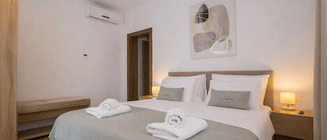 A hotel room with a bed, two bedside tables, a wall-mounted air conditioner, and a door.