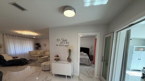 A modern living room with a sofa, a coffee table, and a decorative wall with a religious quote. - White Pearl - Modern 3BR canal home , in Warm Mineral Springs, near beaches (North Port)