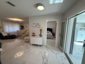 A modern living room with a sofa, a coffee table, and a decorative wall with a religious quote. - White Pearl - Modern 3BR canal home , in Warm Mineral Springs, near beaches (North Port)