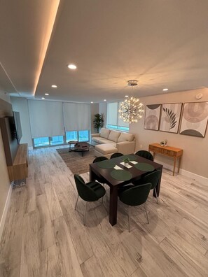 A modern living room with a sofa, a dining table with chairs, a TV, and artwork on the wall. - Luxury Family 3BR Apt in Bay Harbor Islands near Beach, Shops and Dining Area (Bay Harbor Islands)
