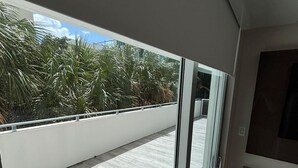 Een balkon met uitzicht op palmbomen, een schuifdeur en een betegelde vloer.