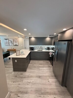 A modern kitchen with grey cabinets, a central island, and a stainless steel refrigerator. - Luxury Family 3BR Apt in Bay Harbor Islands near Beach, Shops and Dining Area (Bay Harbor Islands)