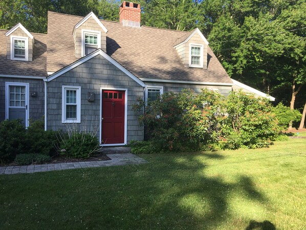 A two-story house with a red front door, a chimney, and a small attached garage.