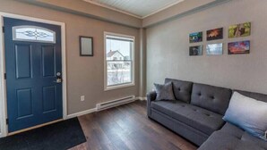 Una sala de estar con una puerta azul oscuro, un sofá gris y una ventana que ofrece vista a una casa.
