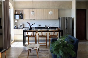 A modern kitchen with wooden cabinets, a stainless steel refrigerator, a microwave, and a coffee maker. There is a dining area with a table and chairs, and a blue sofa. - PENTHOUSE with great view (Guadalajara)