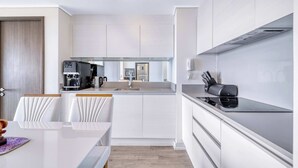 Una cocina moderna con armarios blancos, horno integrado y cafetera.
