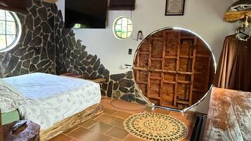 Un dormitorio con una cama, un muro de piedra, techo de madera y una puerta redonda de madera.