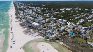 Eine Vogelperspektive auf eine Küstenwohngegend mit Strandhäusern, einem Yachthafen und einem großen Hotel mit mehreren Stockwerken und Balkonen.