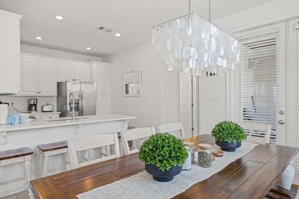 A modern kitchen with white cabinets, stainless steel appliances, and a wooden dining table with potted plants. - “A Little Salt Therapy” in Cassine Village - Seagrove Beach - 3 BR / 3 BA - 2 Pools! (Santa Rosa Beach)