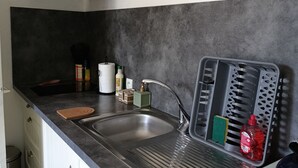 A modern kitchen with a stainless steel sink, a built-in range hood, and a grey countertop. - Hand in hand (Le Houga)