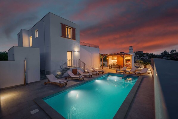 Ein modernes, zweistöckiges Haus mit Swimmingpool, Sitzgelegenheiten im Freien und Kamin.